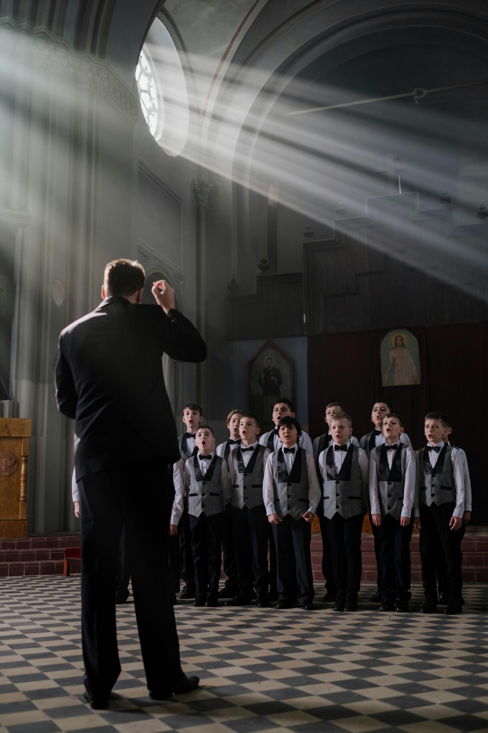 A boys choir rehearsing in a church, led by a conductor, under dramatic light beams.